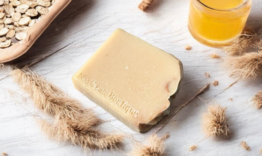 Oat milk and honey artisan soap surrounded by oat and jar of honey on wooden surface