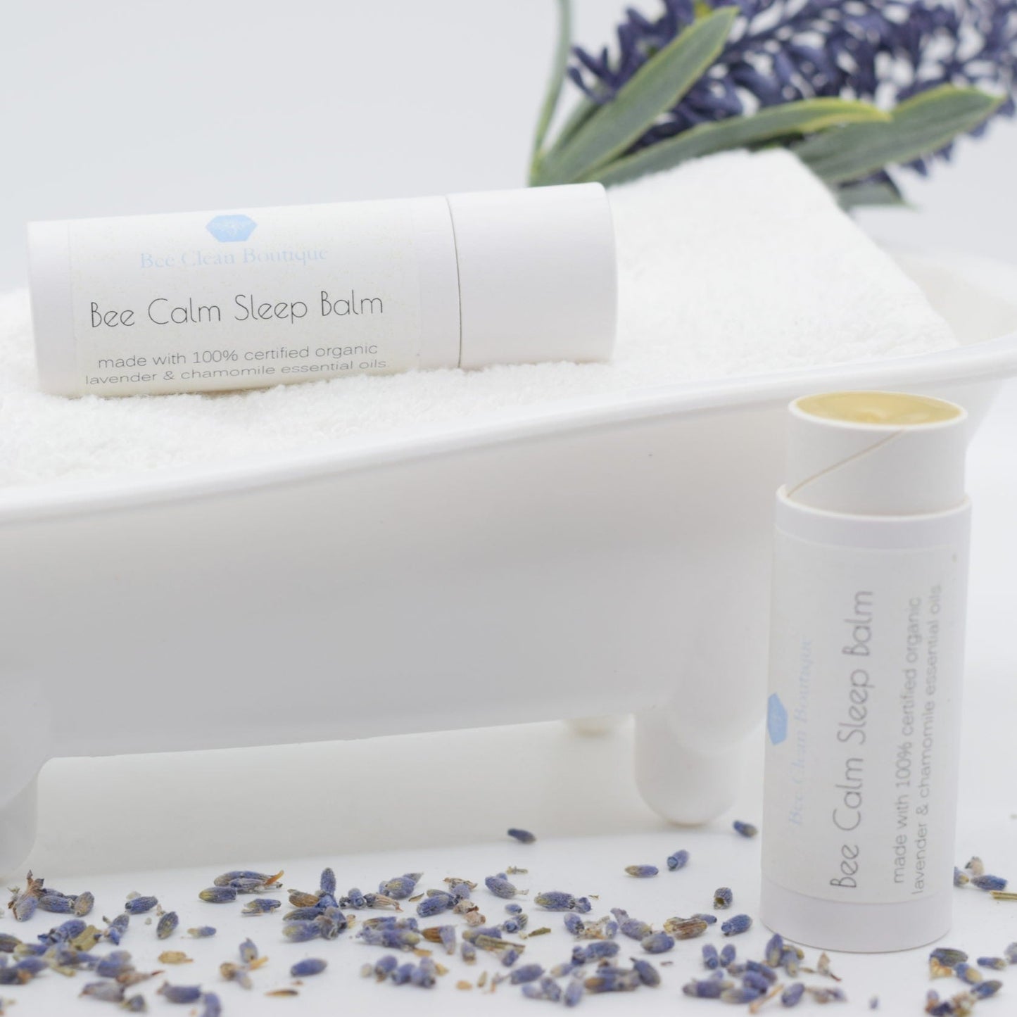 Bee Calm Sleep Balm tubes on display, one lying horizontally on a bath tub-shaped display holder, one vertical on a white surface