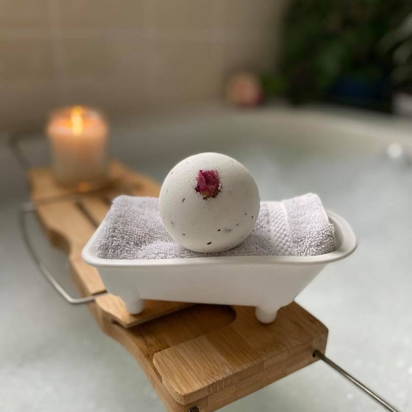 a bath bomb inside a bath tub-shaped holder on a bath caddy; a lit candle is also on the caddy