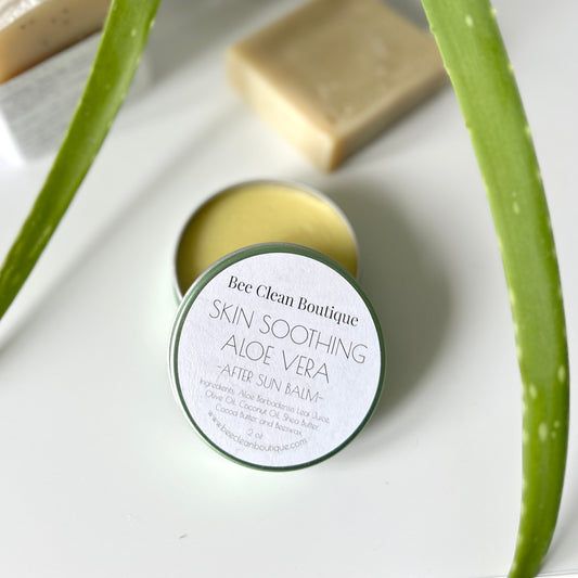 Open tin of skin soothing aloe vera after sun balm on a white surface, surrounded by aloe vera plant