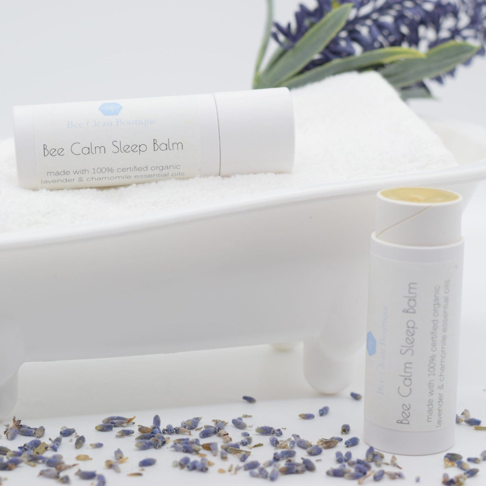 Bee Calm Sleep Balm tubes on display, one lying horizontally on a bath tub-shaped display holder, one vertical on a white surface